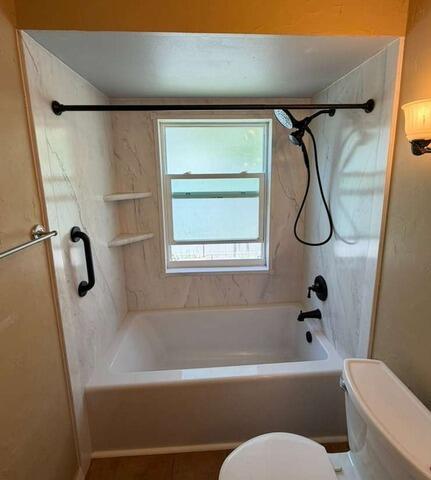 Renovated bathtub with window, black grab rails, and updated surround