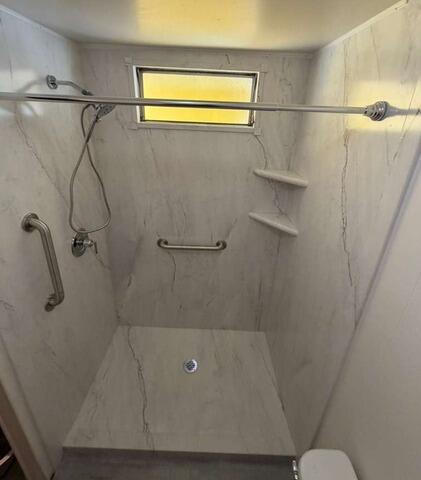 Newly renovated walk-in shower with white and gray marbled wall surround