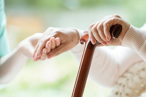 Close-up of hands supporting an elderly person holding a cane